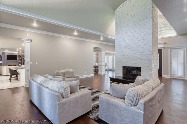 living room featuring decorative columns, a fireplace, dark wood-type flooring, and ornamental molding