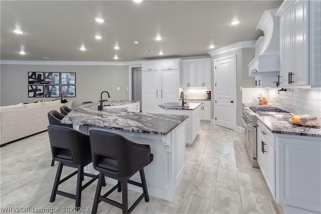 kitchen with white cabinets, custom exhaust hood, a spacious island, and stainless steel stove