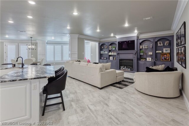 living room with built in shelves, a notable chandelier, crown molding, and sink