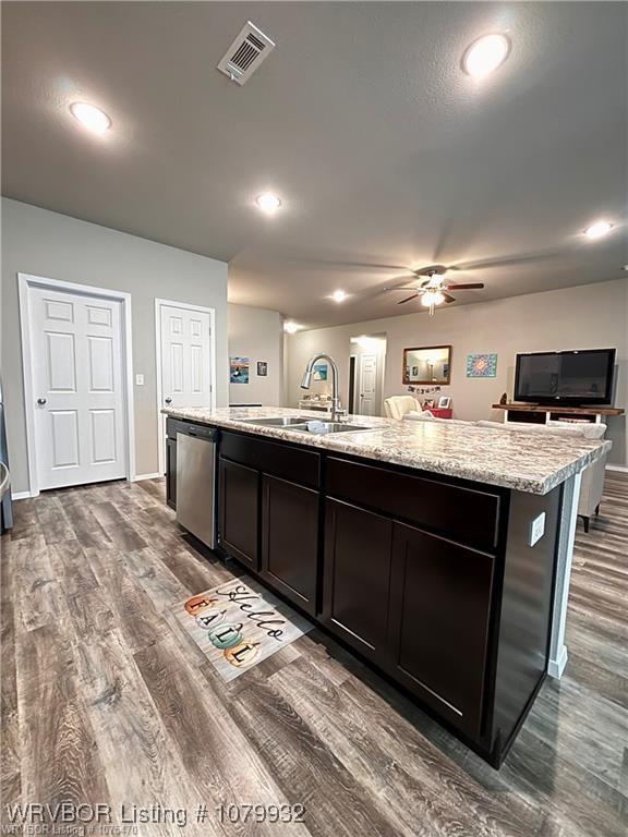 kitchen with stainless steel dishwasher, a sink, dark wood-style floors, an island with sink, and visible vents