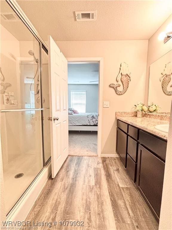 ensuite bathroom with connected bathroom, a stall shower, vanity, wood finished floors, and visible vents
