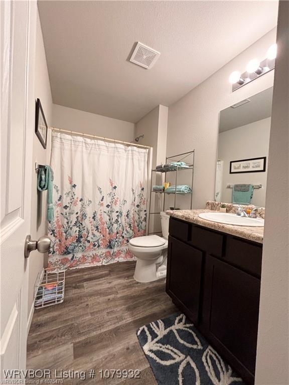 full bath featuring toilet, curtained shower, vanity, wood finished floors, and visible vents