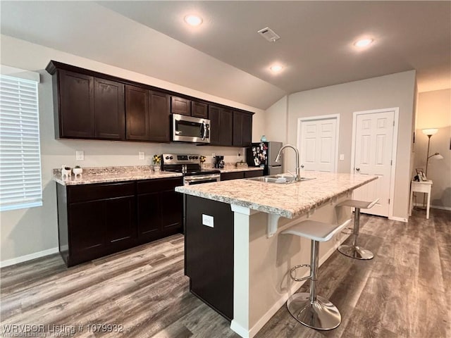 kitchen with a sink, wood finished floors, appliances with stainless steel finishes, a center island with sink, and visible vents