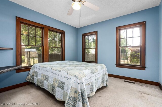 bedroom with multiple windows, ceiling fan, light carpet, and a textured ceiling