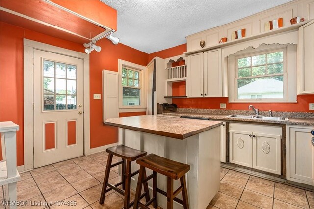 kitchen with light tile patterned flooring, a kitchen bar, sink, a center island, and a textured ceiling