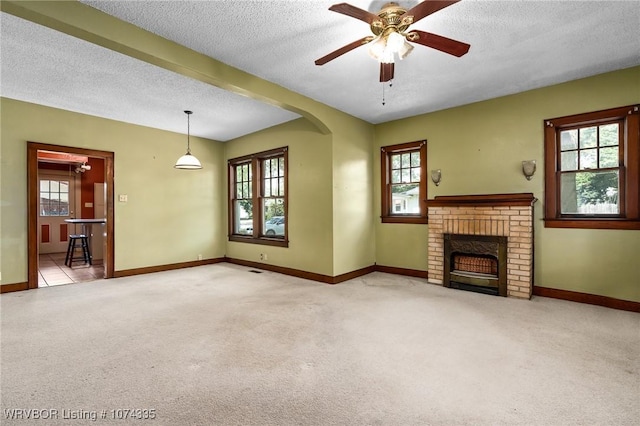 unfurnished living room with a brick fireplace, a wealth of natural light, light colored carpet, and ceiling fan