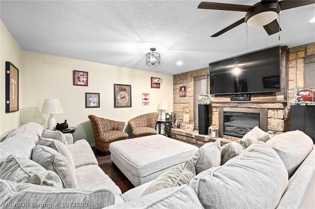 living room featuring ceiling fan, a fireplace, and a textured ceiling