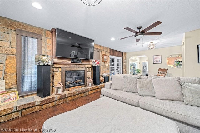 living room with ceiling fan, french doors, a stone fireplace, dark hardwood / wood-style floors, and a textured ceiling