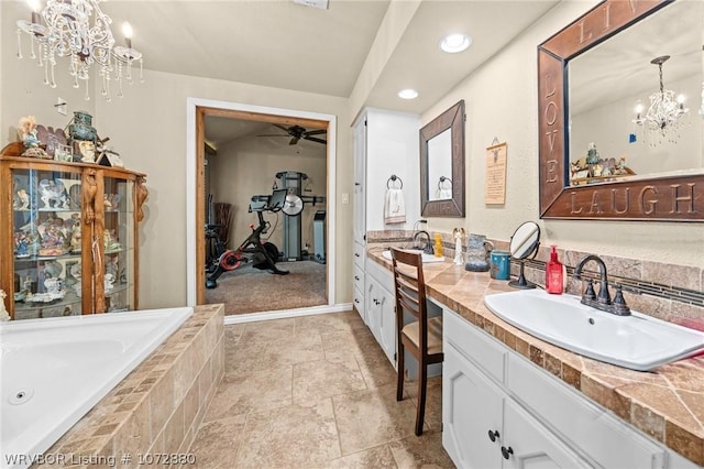 bathroom with ceiling fan with notable chandelier, vanity, and tiled bath