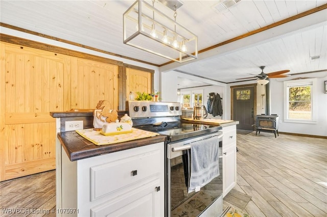 kitchen with stainless steel range with electric stovetop, a wood stove, decorative light fixtures, light hardwood / wood-style floors, and white cabinetry