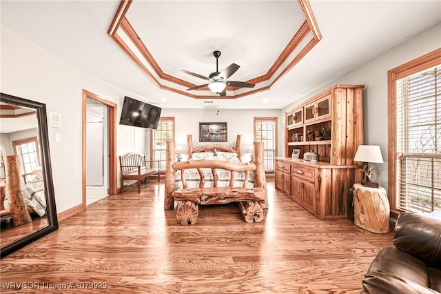 bedroom with a tray ceiling, crown molding, light wood finished floors, and baseboards