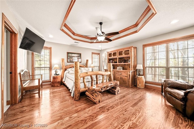 bedroom with a tray ceiling, light wood-style floors, crown molding, baseboards, and a textured ceiling