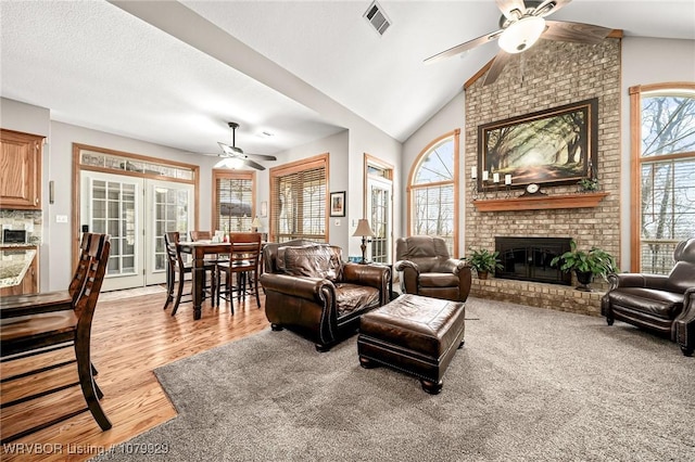 living room with light wood finished floors, visible vents, lofted ceiling, ceiling fan, and a fireplace