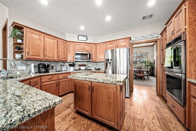 kitchen featuring light stone counters, a sink, stainless steel appliances, light wood-style flooring, and visible vents