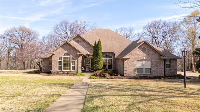 view of front of house with a shingled roof, a front lawn, and brick siding