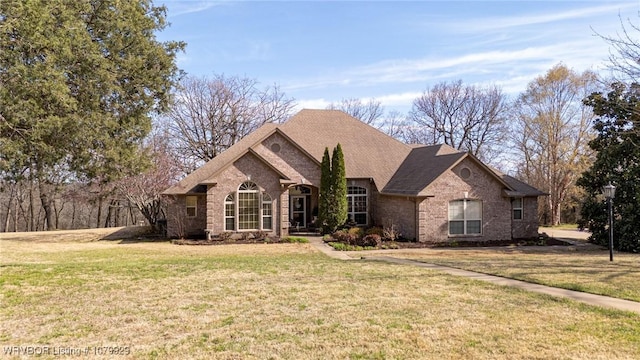 ranch-style house featuring brick siding, a front yard, and roof with shingles