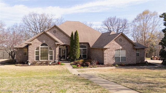 view of front of house with a front lawn, brick siding, and roof with shingles