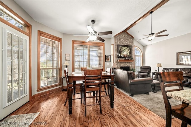 dining room with lofted ceiling with beams, a ceiling fan, wood finished floors, and a fireplace