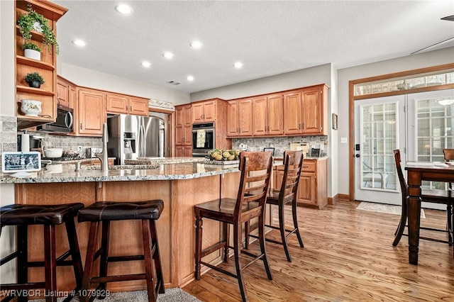 kitchen with open shelves, a textured ceiling, a peninsula, appliances with stainless steel finishes, and light stone countertops