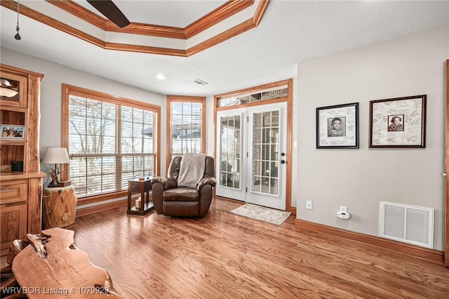 sitting room with wood finished floors, visible vents, a raised ceiling, and ornamental molding