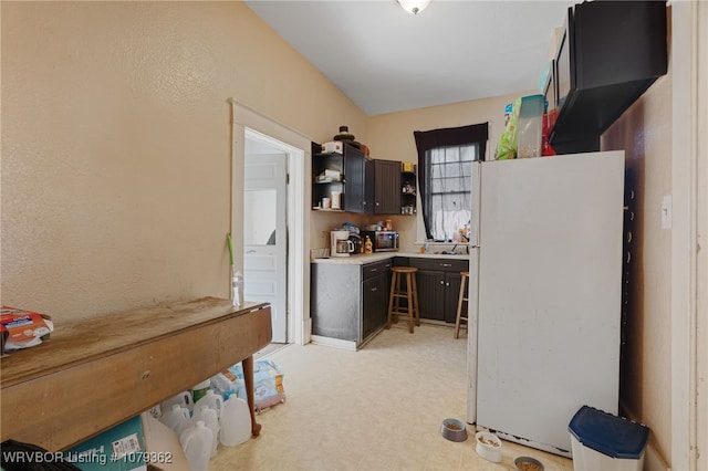 kitchen with stainless steel microwave, light floors, light countertops, freestanding refrigerator, and open shelves