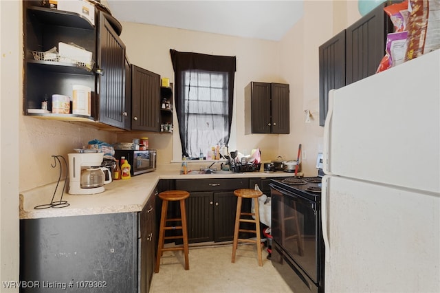 kitchen featuring open shelves, a sink, black range with electric cooktop, freestanding refrigerator, and light countertops