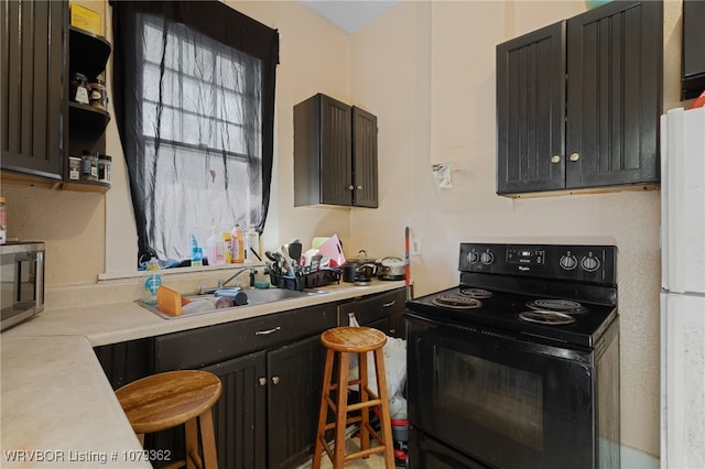 kitchen featuring stainless steel microwave, light countertops, freestanding refrigerator, black / electric stove, and a sink