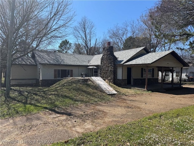 rear view of property with stone siding, a chimney, and roof with shingles