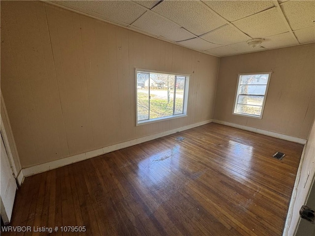 unfurnished room with hardwood / wood-style floors, visible vents, baseboards, and a drop ceiling