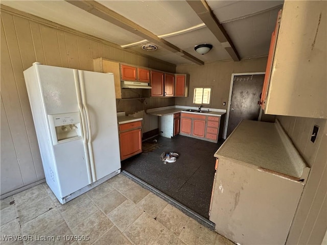 kitchen with under cabinet range hood, beamed ceiling, wood walls, and white refrigerator with ice dispenser