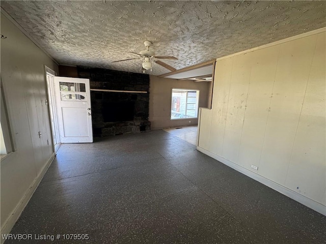 unfurnished living room with a stone fireplace, a textured ceiling, baseboards, and a ceiling fan