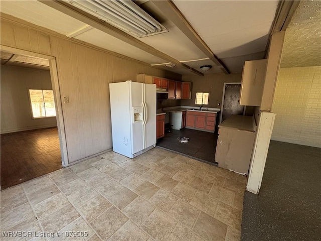 kitchen with under cabinet range hood, white refrigerator with ice dispenser, wood walls, and a sink