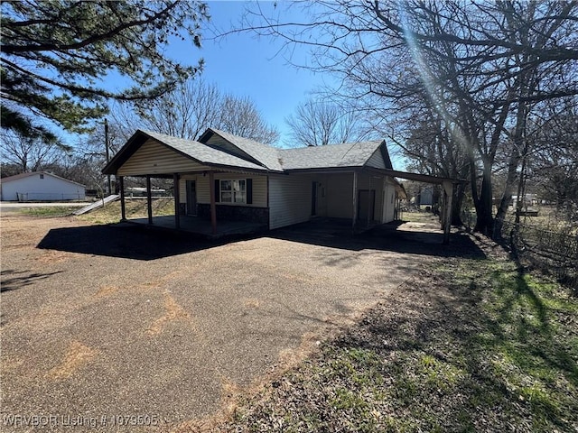 view of side of home with aphalt driveway, a carport, and a shingled roof