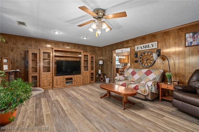 living area with visible vents, a ceiling fan, a textured ceiling, wood walls, and light wood-style flooring