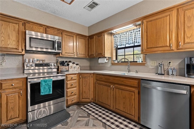kitchen with a sink, light countertops, appliances with stainless steel finishes, and a textured ceiling