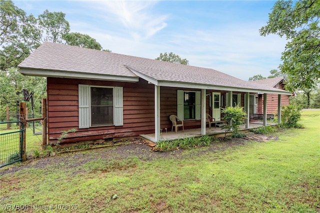 rear view of house with a yard, roof with shingles, and fence