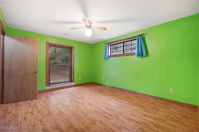 empty room featuring light wood finished floors, visible vents, ceiling fan, a textured ceiling, and baseboards