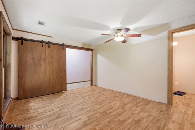 empty room featuring light wood finished floors, a barn door, visible vents, and ceiling fan