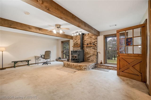 unfurnished living room with ceiling fan, light carpet, visible vents, beamed ceiling, and a wood stove