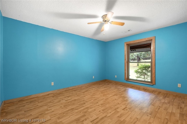 empty room featuring light wood finished floors, a ceiling fan, visible vents, and a textured ceiling