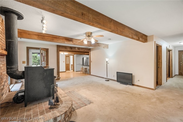 living area featuring baseboards, ceiling fan, beamed ceiling, a wood stove, and carpet flooring