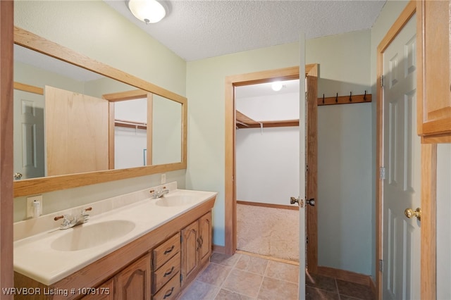 bathroom featuring a textured ceiling, double vanity, a sink, and baseboards