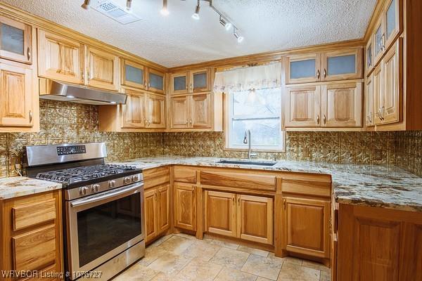 kitchen featuring tasteful backsplash, light stone counters, gas range, a textured ceiling, and sink