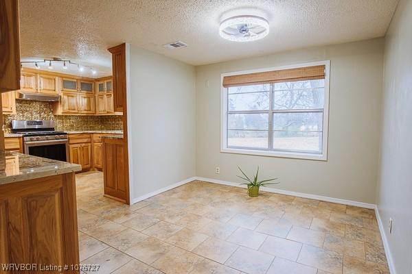 kitchen featuring backsplash, rail lighting, light stone countertops, a textured ceiling, and stainless steel range oven