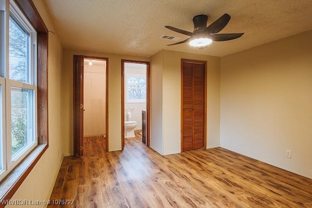 unfurnished bedroom with ensuite bathroom, light hardwood / wood-style flooring, ceiling fan, and a textured ceiling