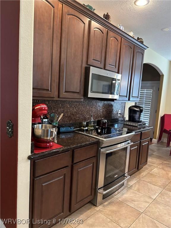 kitchen with stainless steel appliances, a textured ceiling, tasteful backsplash, light tile patterned floors, and dark stone counters