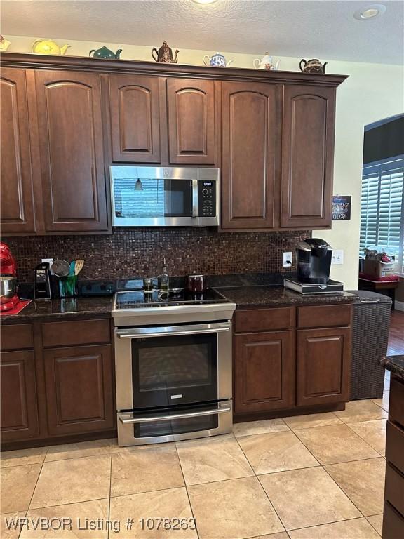 21 Bermuda Ct, Mountain Home, AR 72653 - kitchen with stainless steel appliances, backsplash, light tile patterned flooring, dark brown cabinets, and dark stone counters