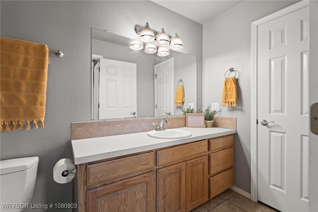 bathroom with toilet, tile patterned flooring, vanity, and a textured wall