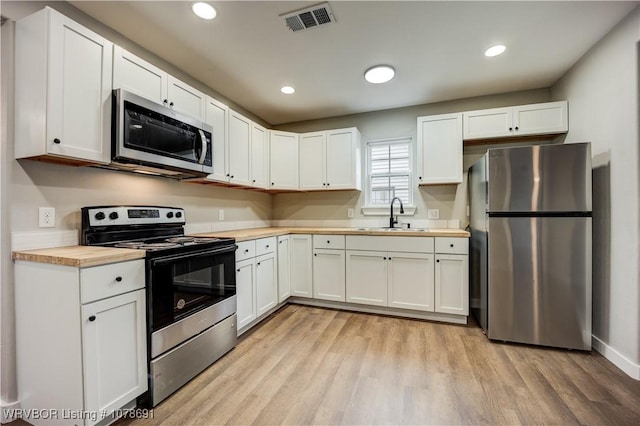 kitchen with sink, butcher block countertops, appliances with stainless steel finishes, white cabinetry, and light wood-type flooring