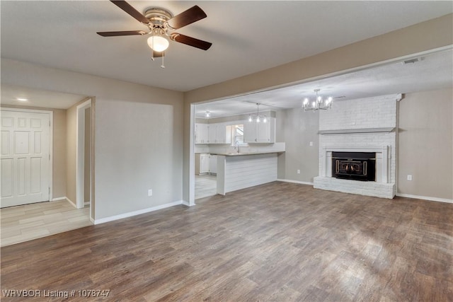 unfurnished living room featuring ceiling fan with notable chandelier, a fireplace, and light wood-type flooring